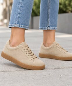 Woman wearing beige suede-look low-top sneakers with gum sole on a city sidewalk, cropped from the knees down