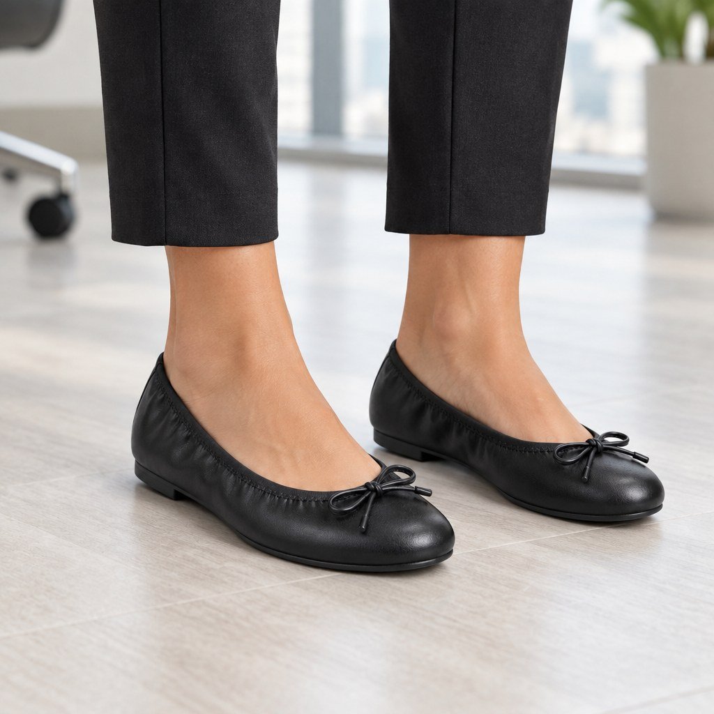 Woman wearing black vegan leather ballet flats with front bow in a bright modern office, cropped from the knees down