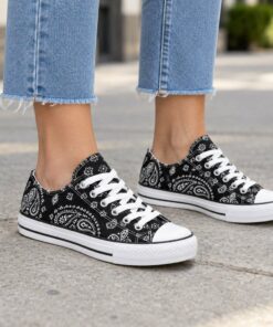 Woman wearing black paisley low-top canvas sneakers on a city sidewalk, cropped from the knees down