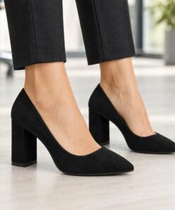 Woman wearing black suede-look pointed toe pumps with 3 inch block heel in a bright modern office, cropped from the knees down