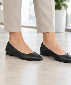 Woman wearing black vegan leather pointed toe flats with low stacked heel in a bright modern office, cropped from the knees down