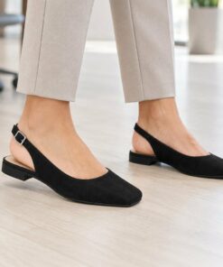 Woman wearing black suede-look square toe slingback flats in a bright modern office, cropped from the knees down