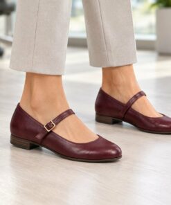 Woman wearing burgundy vegan leather Mary Jane flats in a bright modern office, cropped from the knees down