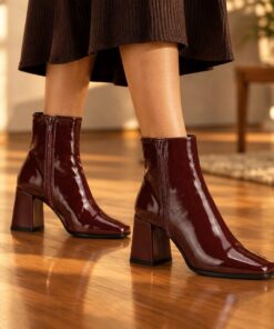 Woman wearing burgundy patent square toe ankle boots with block heel at an evening party, cropped from the knees down