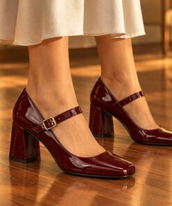 Woman wearing burgundy patent Mary Jane pumps with 2.5 inch block heel at an evening party, cropped from the knees down