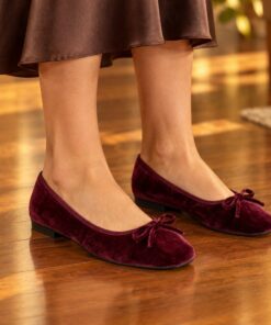 Woman wearing burgundy velvet square toe ballet flats at an evening party, cropped from the knees down