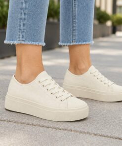 Woman wearing cream low-top platform canvas sneakers on a city sidewalk, cropped from the knees down