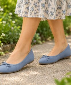 Woman wearing dusty blue suede-look ballet flats with bow on a sunny park path, cropped from the knees down