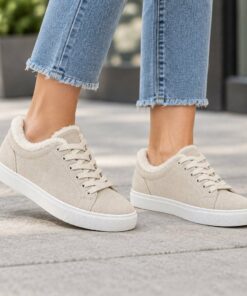 Woman wearing cream suede-look low-top sneakers with faux fur collar on a city sidewalk, cropped from the knees down