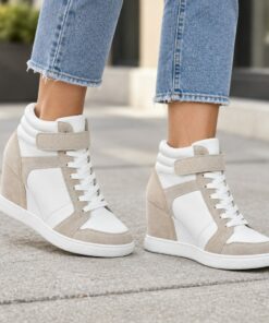 Woman wearing white and beige hidden-wedge high-top sneakers on a city sidewalk, cropped from the knees down