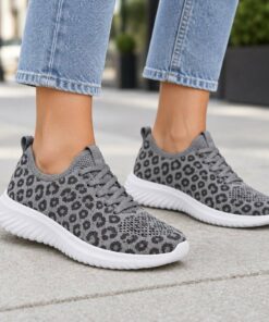 Woman wearing grey leopard print knit mesh sneakers on a city sidewalk, cropped from the knees down