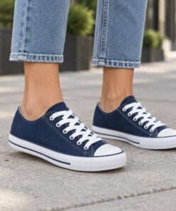 Woman wearing navy blue classic low-top canvas sneakers on a city sidewalk, cropped from the knees down