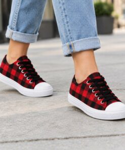 Woman wearing red buffalo check low-top canvas sneakers with cuffed jeans on a city sidewalk, cropped from the knees down