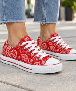 Woman wearing red paisley low-top canvas sneakers on a city sidewalk, cropped from the knees down