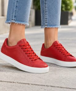 Woman wearing red smooth vegan leather low-top sneakers on a city sidewalk, cropped from the knees down