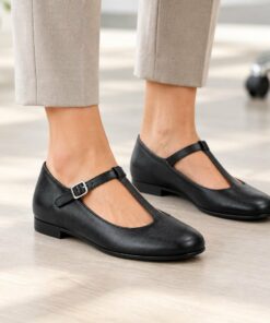 Woman wearing black vegan leather T-strap Mary Jane flats in a bright modern office, cropped from the knees down