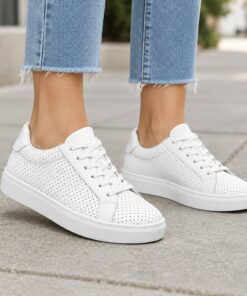 Woman wearing white perforated vegan leather low-top sneakers on a city sidewalk, cropped from the knees down
